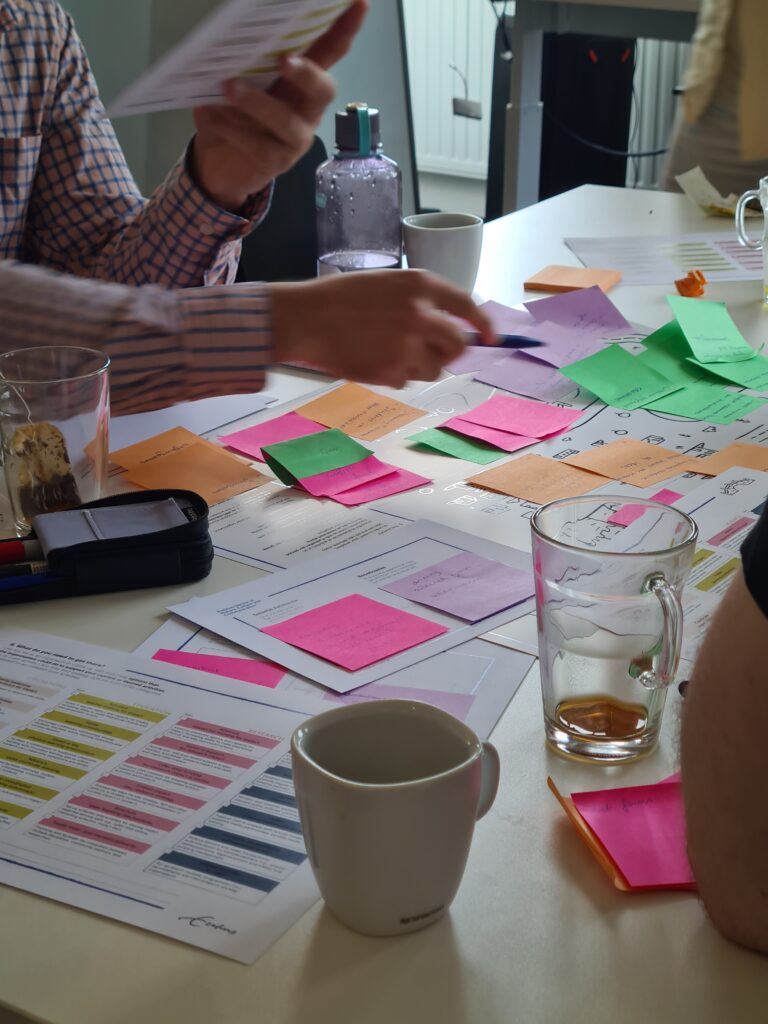 Photo of a busy table with templates and sticky notes and a person gesturing above them. 