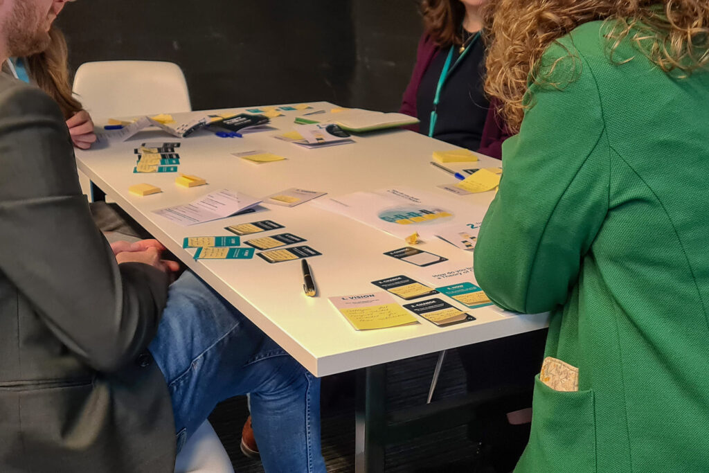 A photo of a group of people surrounding a table while playing Journey of Progress. 